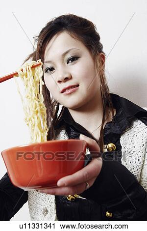 Stock Image - Close-up of a young woman holding noodles with a pair of chopsticks. Fotosearch