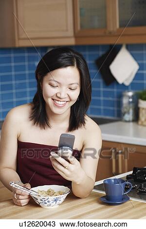 Stock Image - Close-up of a young woman looking at a mobile phone smiling. Fotosearch