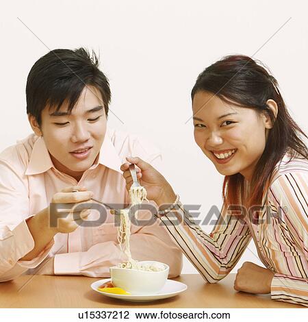 Stock Image - Close-up of two young couples eating noodles and smiling. Fotosearch