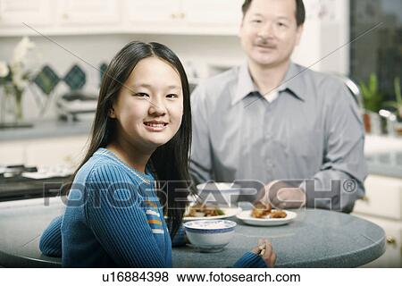 Stock Photo - Portrait of a girl sitting at a table with her father. Fotosearch