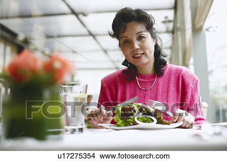 Picture - Portrait of a mature woman seated at the table in a restaurant smiling. Fotosearch