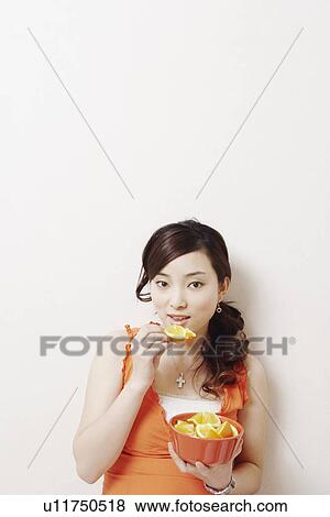 Stock Photo - Portrait of a young woman eating slices of orange. Fotosearch