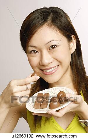 Stock Image - Portrait of a young woman eating chocolates. Fotosearch