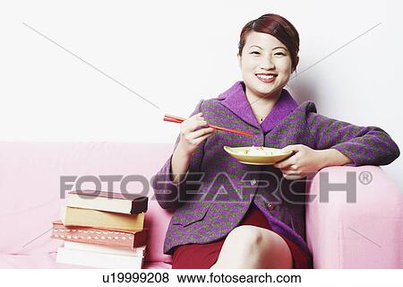 Stock Photo - Portrait of a young woman eating with chopsticks. Fotosearch