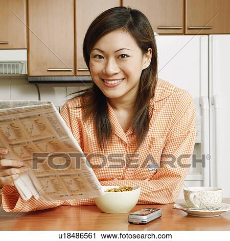 Portrait of a young woman holding a newspaper at a kitchen counter View Large Photo Image Stock Image - Portrait of a young woman holding a newspaper at a kitchen counter. Fotosearch