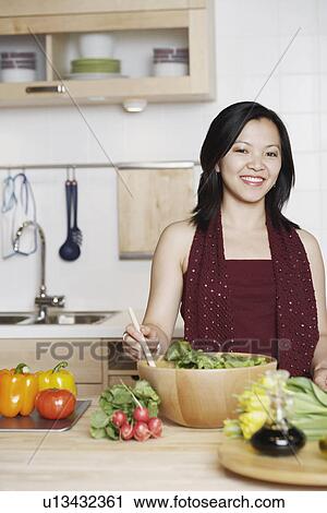 Stock Image - Portrait of a young woman preparing food in the kitchen smiling. Fotosearch