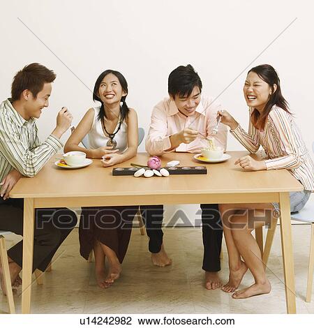 Stock Image - Two young couples eating noodles and smiling. Fotosearch