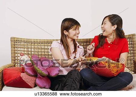 Two young women sitting together on a couch and eating sweet food View Large Photo Image Stock Photo - Two young women sitting together on a couch and eating sweet food. Fotosearch