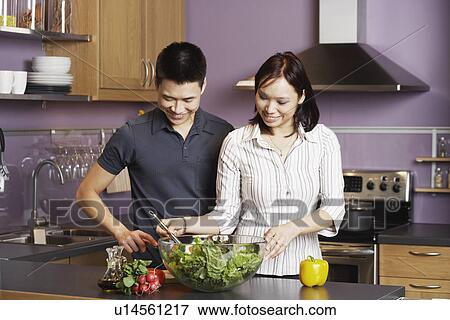 Young man standing looking at a young woman preparing food View Large Photo Image Stock Photo - Young man standing looking at a young woman preparing food. Fotosearch