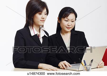 Stock Image - Close-up of two businesswomen in front of a laptop. Fotosearch