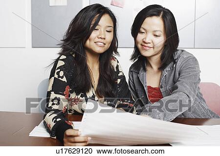 Stock Image - Close-up of two businesswomen reading documents. Fotosearch