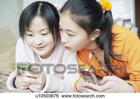 Stock Photograph - Close-up of two sisters using mobile phones. Fotosearch