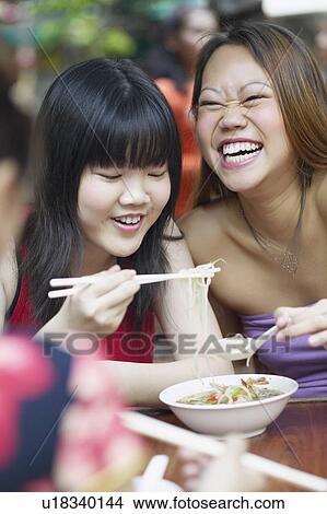 Close-up of two young women eating noodles with chopsticks View Large Photo Image Picture - Close-up of two young women eating noodles with chopsticks. Fotosearch