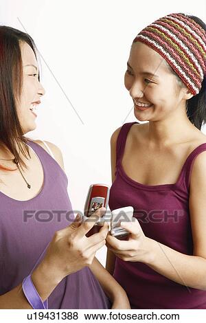 Close-up of two young women holding mobile phones and looking at each other View Large Photo Image Stock Photo - Close-up of two young women holding mobile phones and looking at each other. Fotosearch