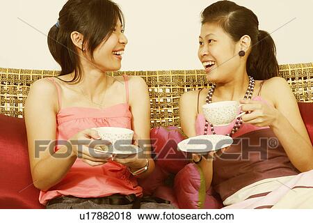 Close-up of two young women holding tea cups on a couch and smiling View Large Photo Image Stock Photo - Close-up of two young women holding tea cups on a couch and smiling. Fotosearch