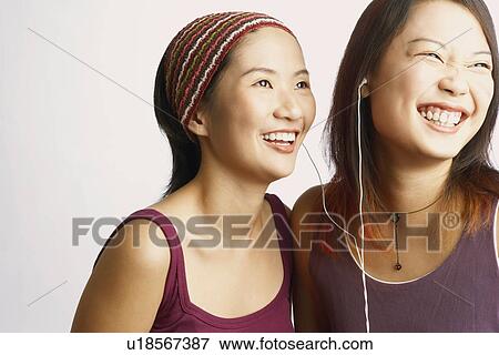 Stock Photo - Close-up of two young women listening to music and smiling. Fotosearch