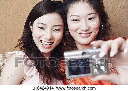 Picture - Close-up of two young women taking a photograph of themselves. Fotosearch
