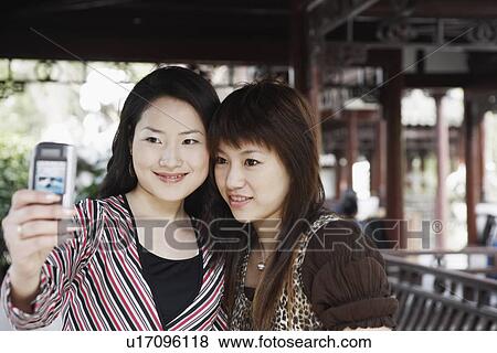 Stock Photo - Close-up of two young women taking a photograph of themselves. Fotosearch