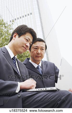 Picture - Low angle view of two businessmen using a laptop. Fotosearch