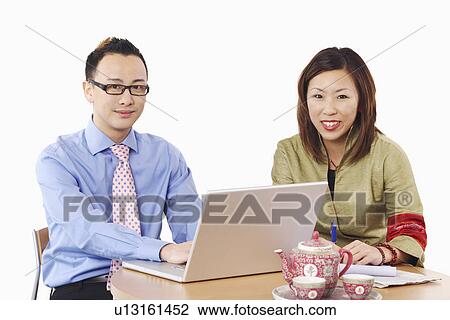 Portrait of a businessman and a businesswoman sitting in front of a laptop View Large Photo Image Stock Image - Portrait of a businessman and a businesswoman sitting in front of a laptop. Fotosearch