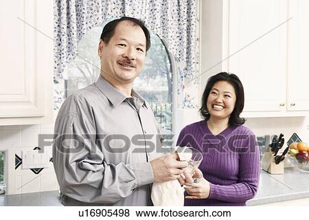 Stock Photo - Portrait of a senior man cleaning a glass with a mature woman standing behind her. Fotosearch