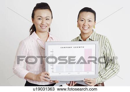 Stock Image - Portrait of two businesswomen holding a progress report and smiling. Fotosearch