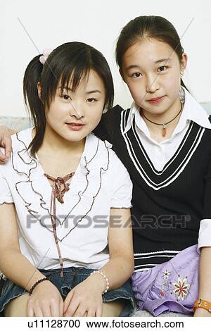 Stock Image - Portrait of two young women sitting together on a couch. Fotosearch