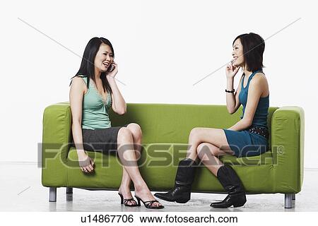 Side profile of two young women sitting on a couch talking on mobile phones View Large Photo Image Stock Photograph - Side profile of two young women sitting on a couch talking on mobile phones. Fotosearch