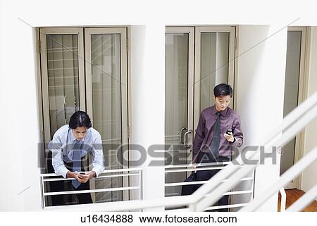 Two businessmen holding mobile phones View Large Photo Image Stock Photo - Two businessmen holding mobile phones. Fotosearch