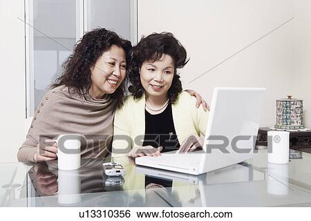 Stock Photograph - Two mature women using a laptop smiling. Fotosearch