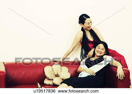Stock Photograph - Two mid adult women sitting on a couch and smiling. Fotosearch