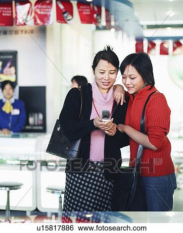 Stock Photograph - Two young women looking at a mobile phone. Fotosearch
