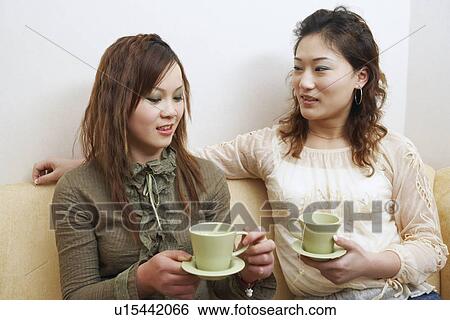 Two young women sitting on a couch holding tea cups View Large Photo Image Stock Photograph - Two young women sitting on a couch holding tea cups. Fotosearch