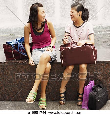 Picture - Two young women talking near a fountain. Fotosearch