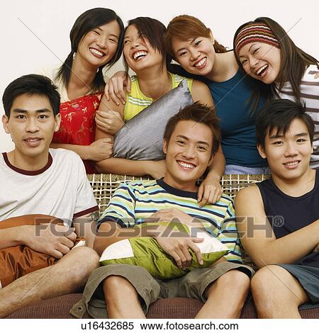 Stock Photography - Close-up of three young men sitting on a couch with four women standing behind them. Fotosearch