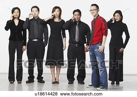 Stock Photo - Portrait of a young man standing with a group of business executives using mobile phones. Fotosearch