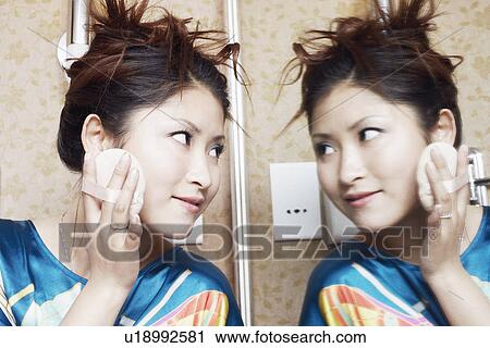 Stock Image - Close-up of a teenage girl looking into a mirror applying face powder. Fotosearch