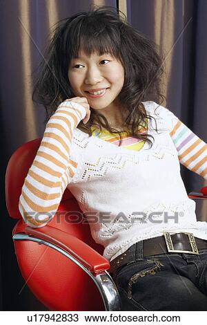 Stock Image - Close-up of a young woman sitting on an armchair smiling. Fotosearch