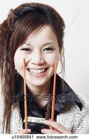 Stock Image - Portrait of a young woman holding a pair of chopsticks. Fotosearch