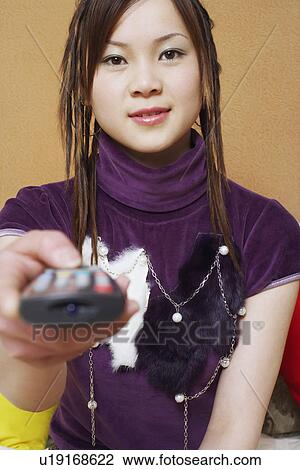 Stock Image - Portrait of a young woman holding a remote control. Fotosearch