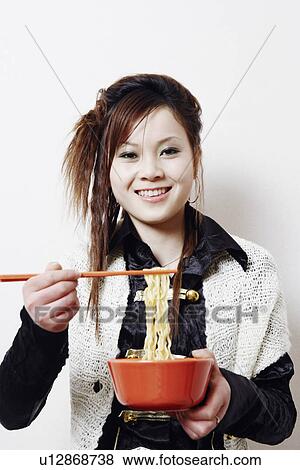 Stock Photo - Portrait of a young woman holding noodles with a pair of chopsticks. Fotosearch