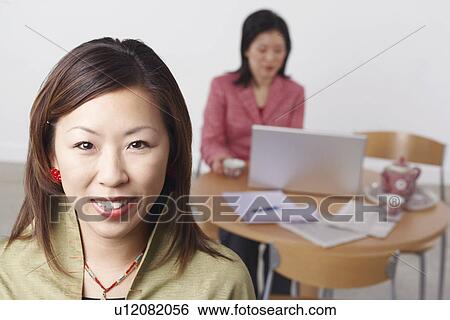 Stock Photograph - Portrait of a businesswoman smiling with another businesswoman using a laptop behind her. Fotosearch