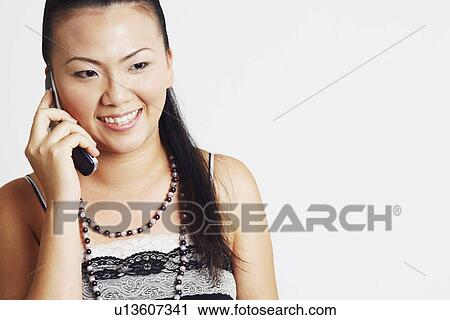 Stock Image - Close-up of a young woman smiling and talking on a mobile phone. Fotosearch