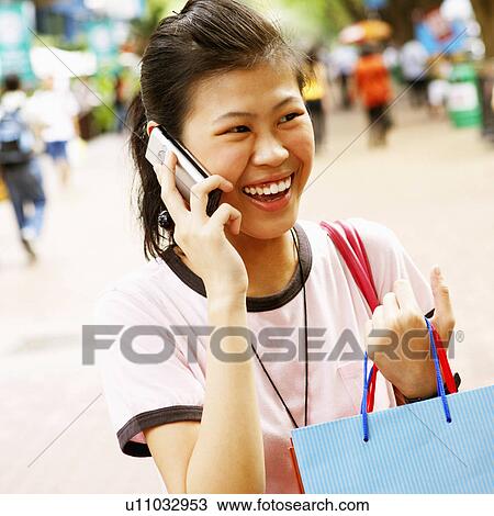 Stock Image - Close-up of a young woman talking on a mobile phone and carrying a shopping bag. Fotosearch