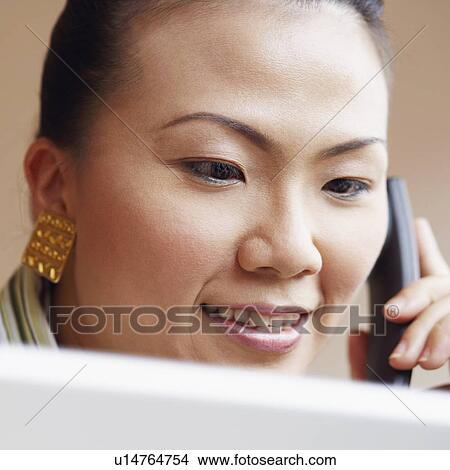 Picture - Close-up of a young woman talking on the telephone and looking at a laptop. Fotosearch