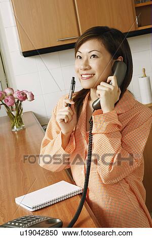 Stock Image - Close-up of a young woman using a telephone in the kitchen. Fotosearch