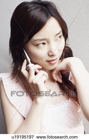 Stock Photo - Close-up of a young woman using a mobile phone looking away. Fotosearch