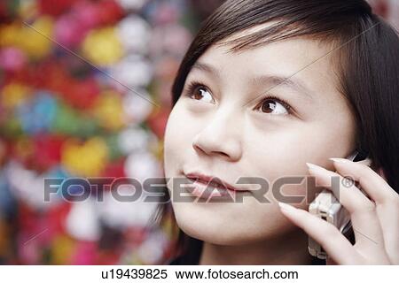 Stock Photography - Close-up of a young woman using a mobile phone looking away. Fotosearch