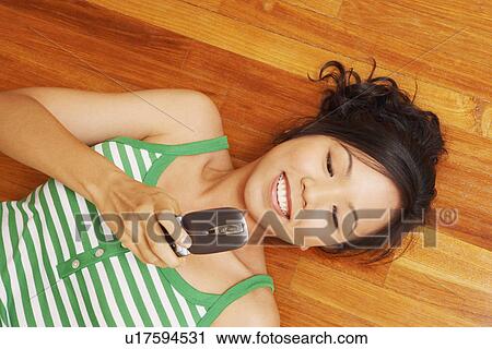 Stock Image - High angle view of a young woman lying on a hardwood floor and holding a mobile phone. Fotosearch