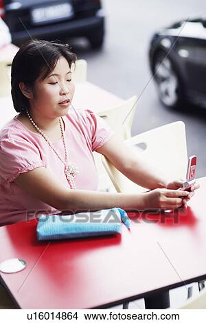 Picture - High angle view of a young woman sitting at a sidewalk cafe and holding a mobile phone. Fotosearch